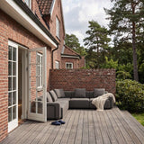 sackit dark grey five seat corner sofa on a wooden terrace beside a brick house and garden trees with a draped throw