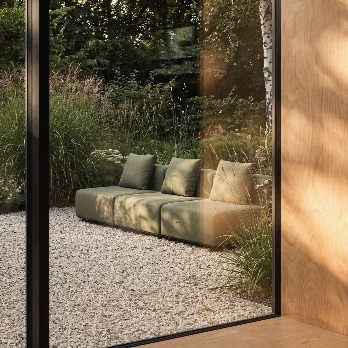 Olive green three seat outdoor lounge sofa with cushions in a landscaped garden viewed through a glass wall by sackit Danish furniture designers