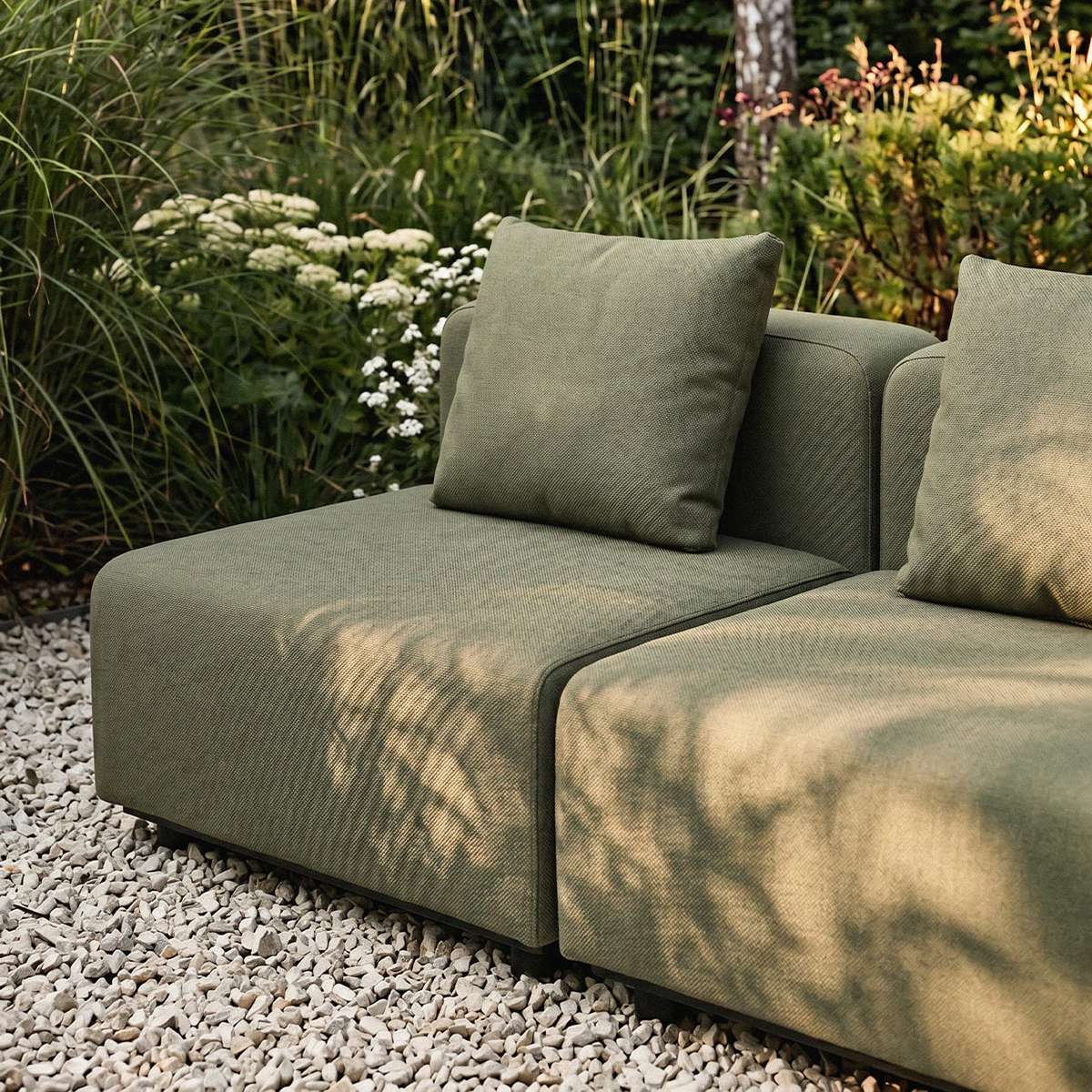 sackit outdoor two seater lounge sofa in olive green fabric with cushions on a gravel patio surrounded by lush Nordic garden planting
