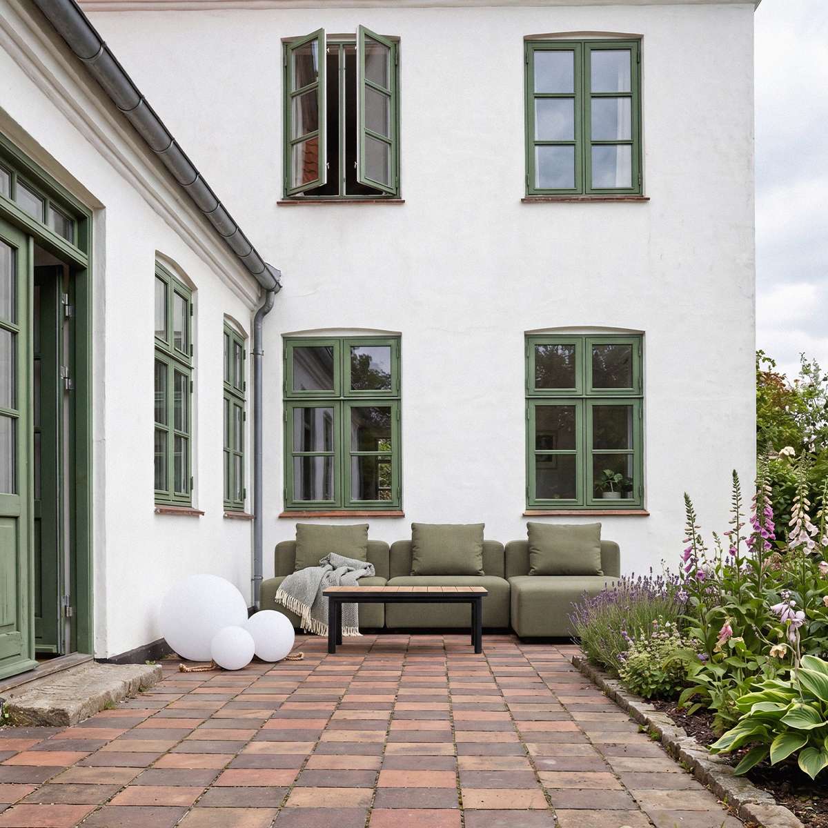 Olive green three seat outdoor lounge sofa with clean Scandinavian lines, styled with a black coffee table in a flower filled courtyard by sackit