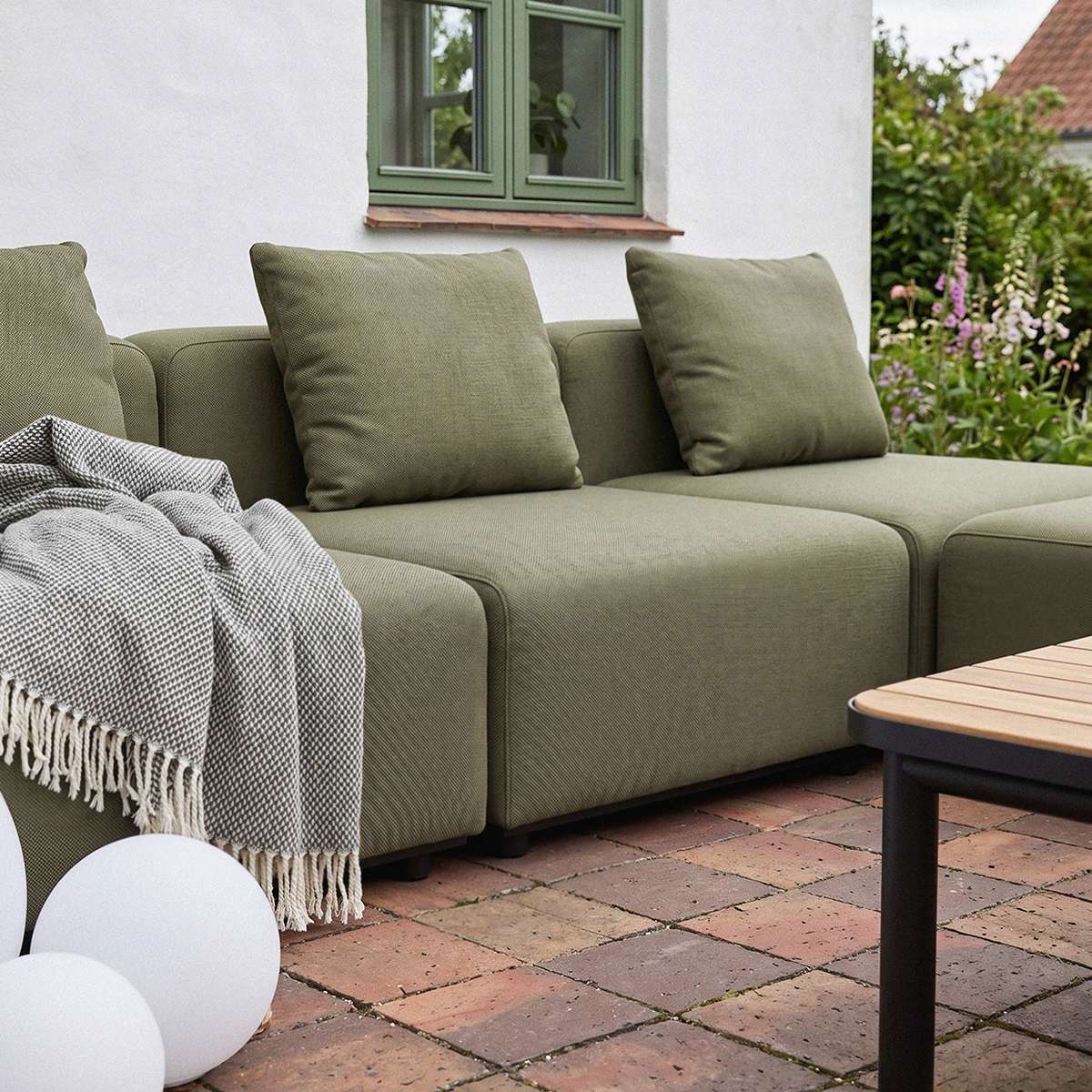 sackit olive green modular outdoor corner sofa with cushions and throw on a brick patio in a garden setting