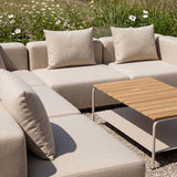 Beige modular outdoor corner sofa with soft cushions and a slatted wood coffee table in a sunny Nordic garden setting