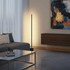 Slim black floor lamp with vertical frosted LED strip and marble base standing on a white floor.