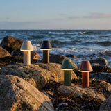 Four cordless outdoor table lamps by sackit on coastal rocks with waves in the background in soft evening light