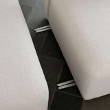Close up of a light fabric sofa with visible metal joining brackets between cushioned sections on a dark tiled floor from sackit