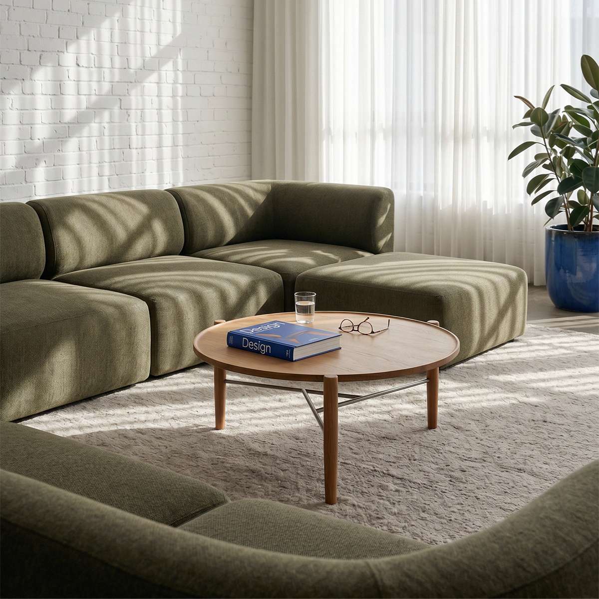 Olive green Fjord Sofa seat section in a calm Scandinavian living room with a round wooden coffee table and bright natural light from sheer curtains by sackit