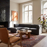 Dark gray Fjord sofa with left chaise in a bright Scandinavian living room with a patterned rug wood coffee table and indoor plant by tall windows from sackit