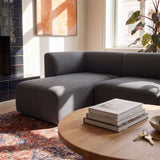 Dark gray sackit Fjord Sofa with left chaise in a sunlit Scandinavian living room beside a round wooden coffee table and patterned rug