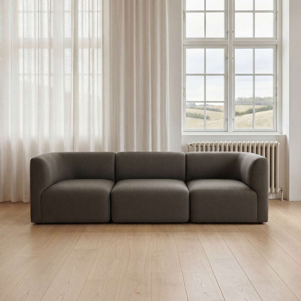 Dark gray sackit fjord sofa seat section with soft rounded lines in a bright Scandinavian interior with tall windows and wood flooring