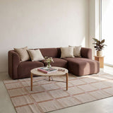 Brown Scandinavian chaise sofa with soft cushions beside a round coffee table on a patterned rug in a bright living room from sackit
