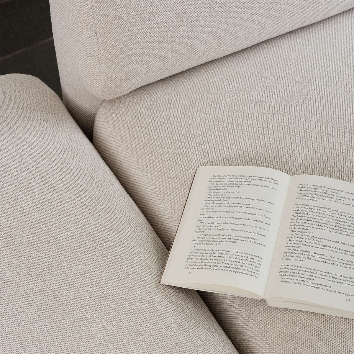 Close view of a light fabric Fjord Sofa with an open book resting on its soft cushions showcasing calm Scandinavian design by sackit