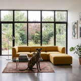 Mustard yellow sackit three seater sofa with chaise in a bright Scandinavian living room featuring a patterned rug large windows and a seated dog