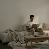 Scandinavian corner sofa with an open end styled with a soft throw as a man reads beside a wooden coffee table in a calm living room by sackit