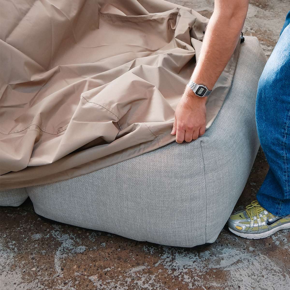 Person fitting a sand water repellent cover over a grey Soft Sofa outdoor lounger from sackit to protect it from wind and weather