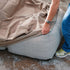 Person fitting a sand water repellent cover over a grey Soft Sofa outdoor lounger from sackit to protect it from wind and weather