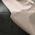 Close view of a sand colored weather resistant cover fitted over a dark Cobana outdoor sofa showing its smooth fabric and reinforced stitched seam from sackit