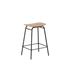 Low bar stool with natural oak veneer seat and black powder-coated steel frame.