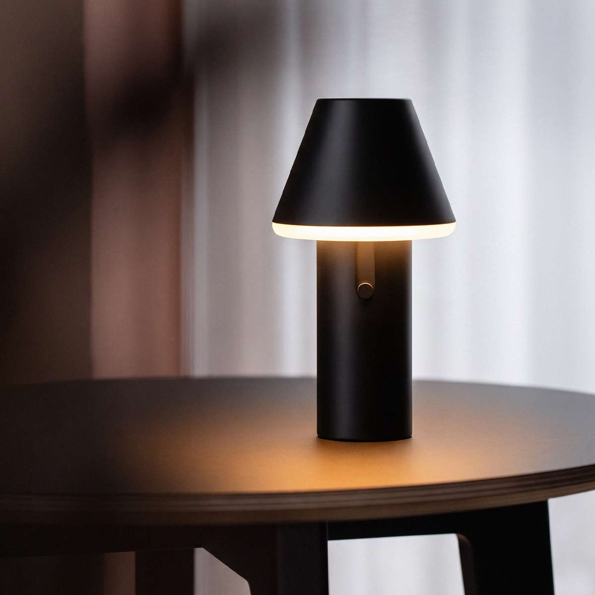 Black Cone cordless table lamp by sackit glowing warmly on a dark wooden table in a modern interior for indoor and outdoor use