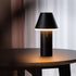 Black Cone cordless table lamp by sackit glowing warmly on a dark wooden table in a modern interior for indoor and outdoor use
