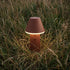 sackit Cone cordless outdoor table lamp in brown powder coated aluminium glowing warmly among tall Nordic grass for weather resistant illumination