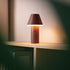 sackit cordless brown table lamp glowing warmly on a wooden shelf with a conical shade and soft ambient light indoors