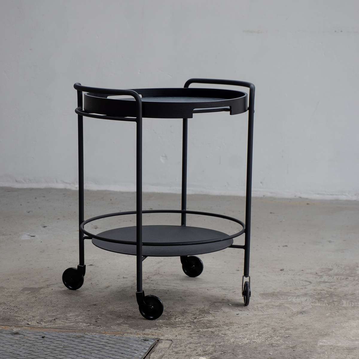 Serving table with black lacquered steel frame and natural oak round serving tray on top in a room setting