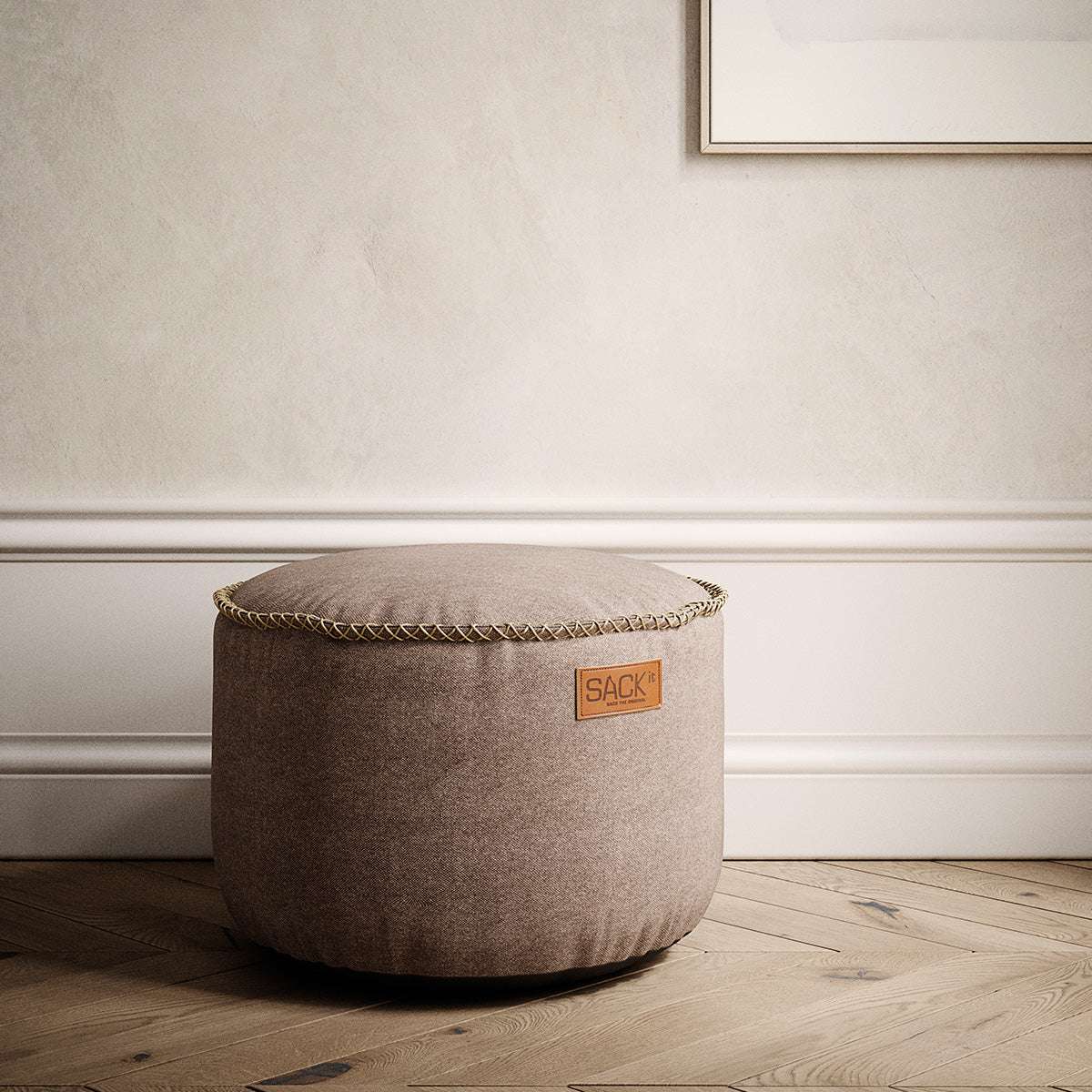 Brown canvas indoor pouf with a rounded shape and decorative stitched edge on a wooden floor in a calm neutral interior by sackit