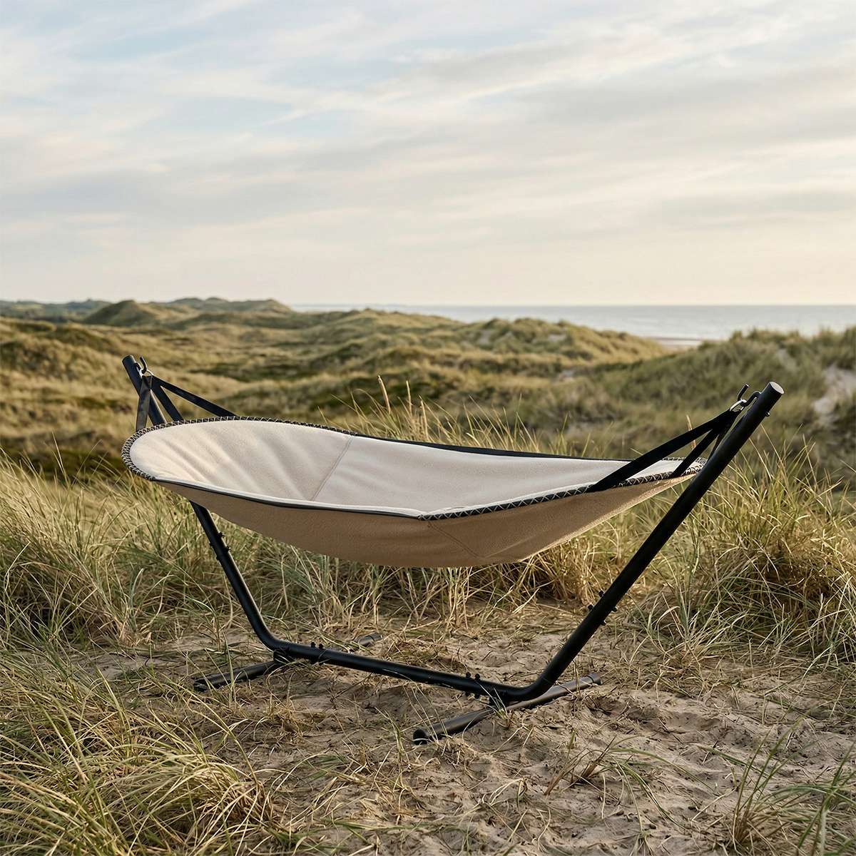 sackit Cobana hammock with cream fabric and black stand resting among coastal dunes beside the sea on a calm Nordic day