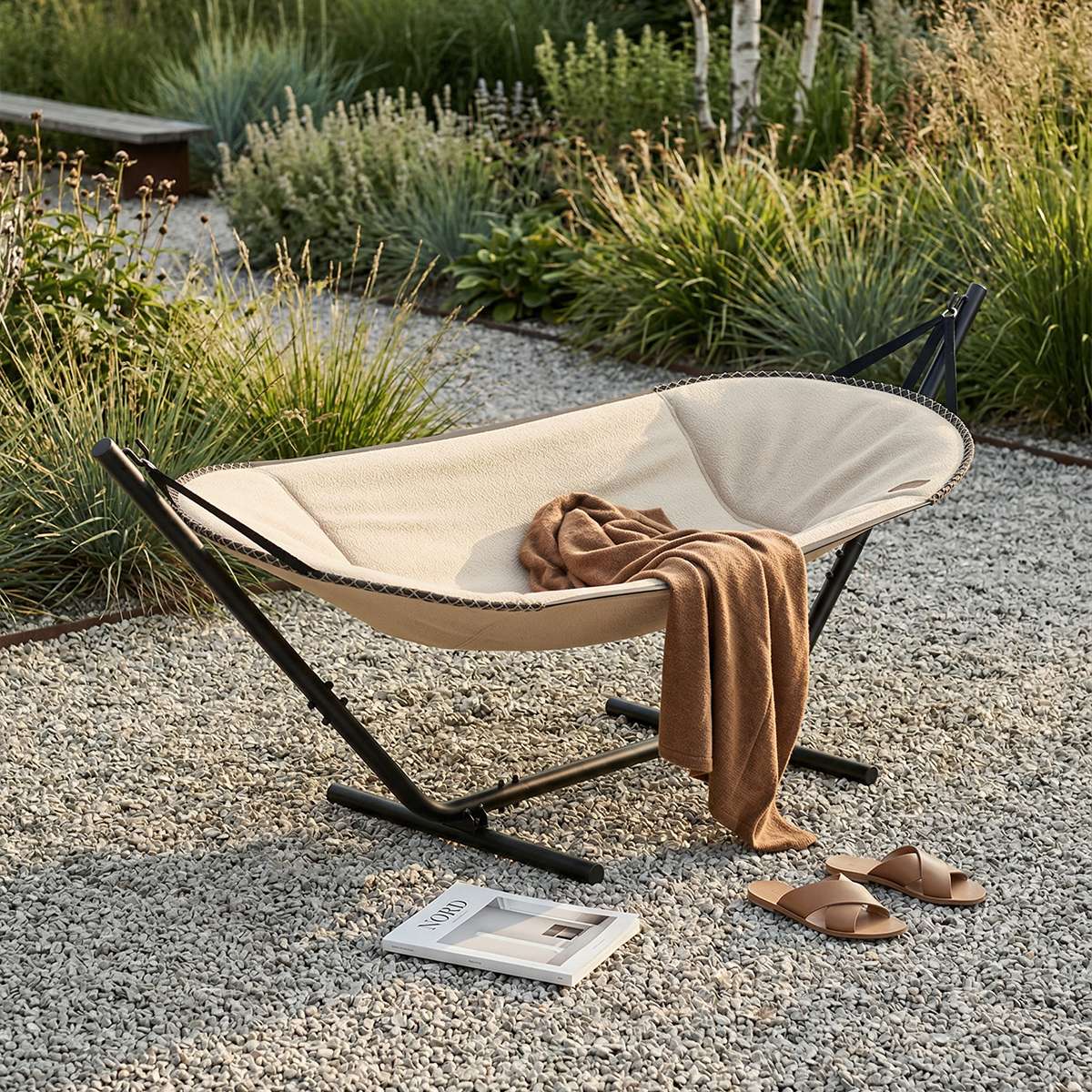 Cream Cobana hammock by sackit set in a landscaped garden with a soft brown blanket and sandals nearby for relaxed outdoor lounging