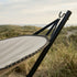 sackit Cobana hammock in light grey textile with black supports set among coastal dune grass beneath a soft overcast sky