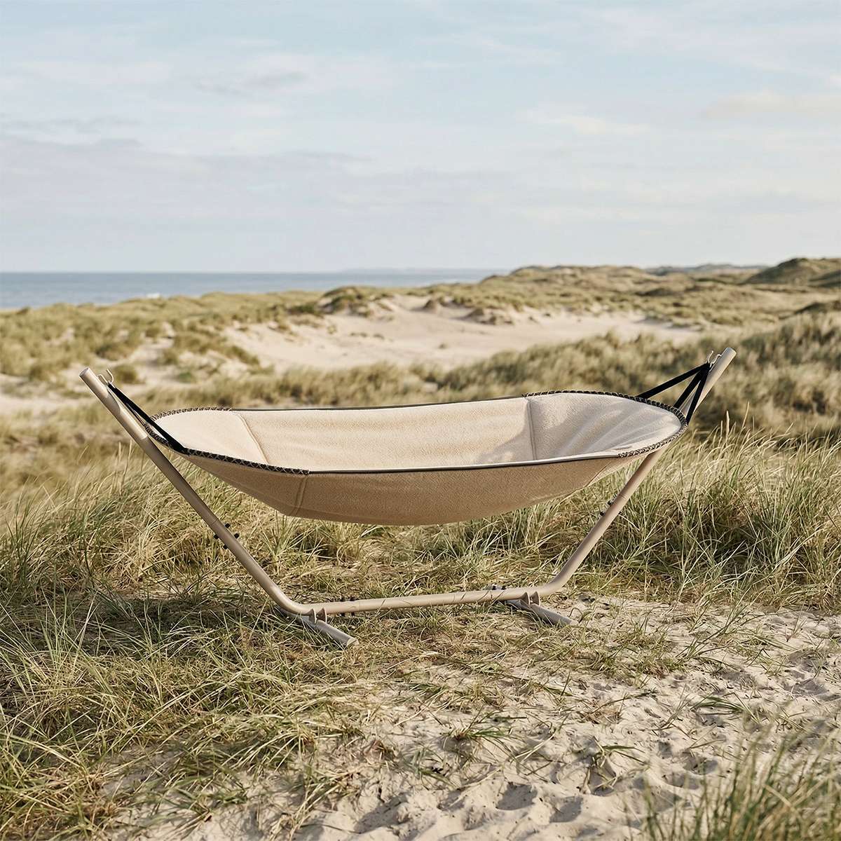sackit Cobana hammock in soft beige fabric on a stand among coastal dunes and grass for comfortable outdoor lounging
