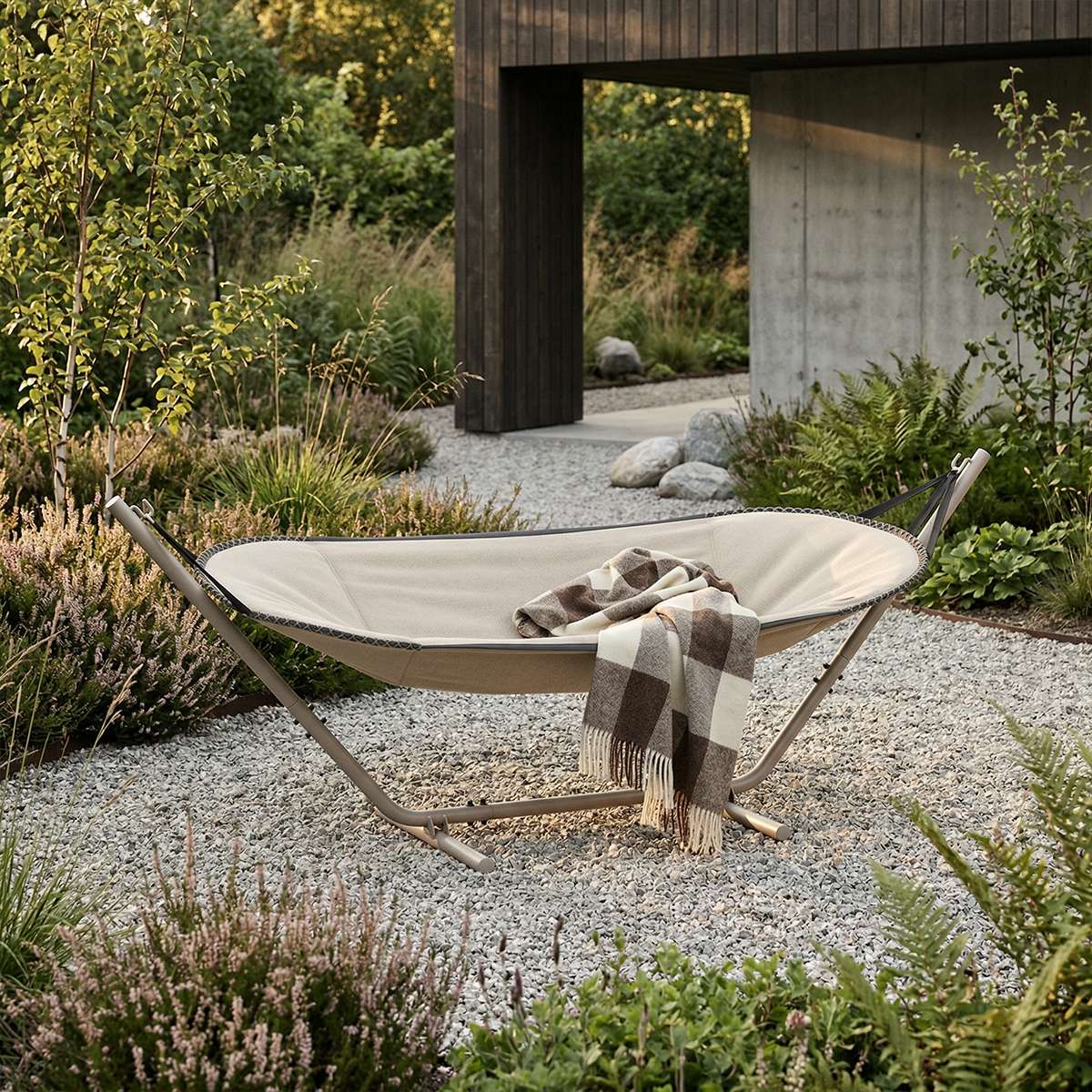 Cream outdoor hammock with a soft patterned blanket in a landscaped garden beside a modern Nordic style home for comfortable summer lounging