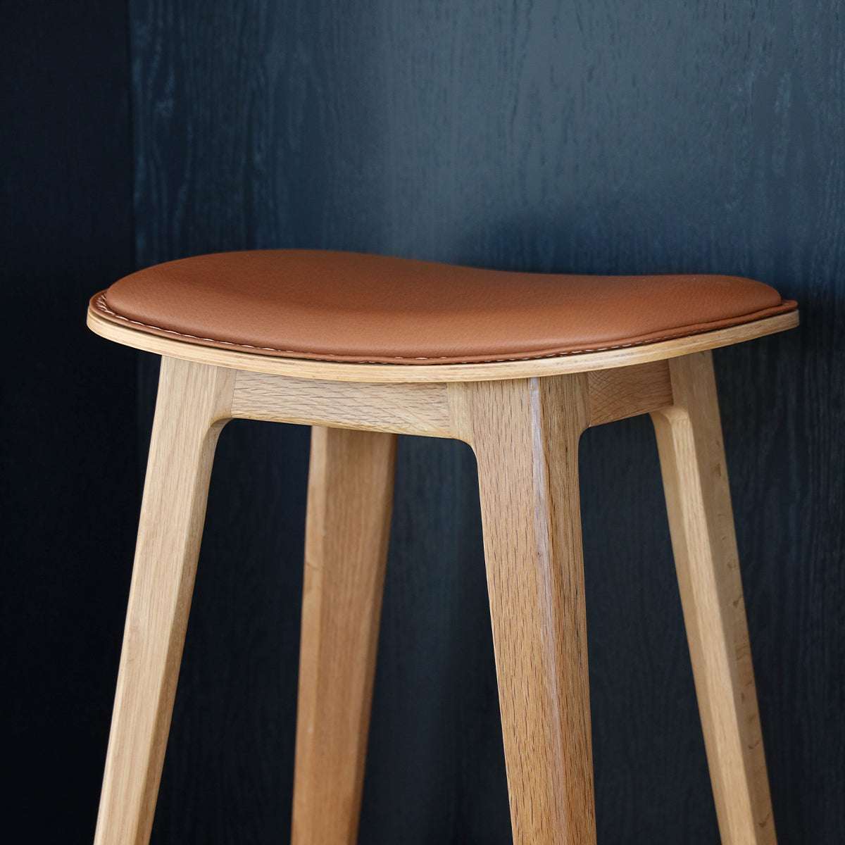 Nordic bar stool in Terra Black leather with oak wood and cross-stitch details, 73 cm height.