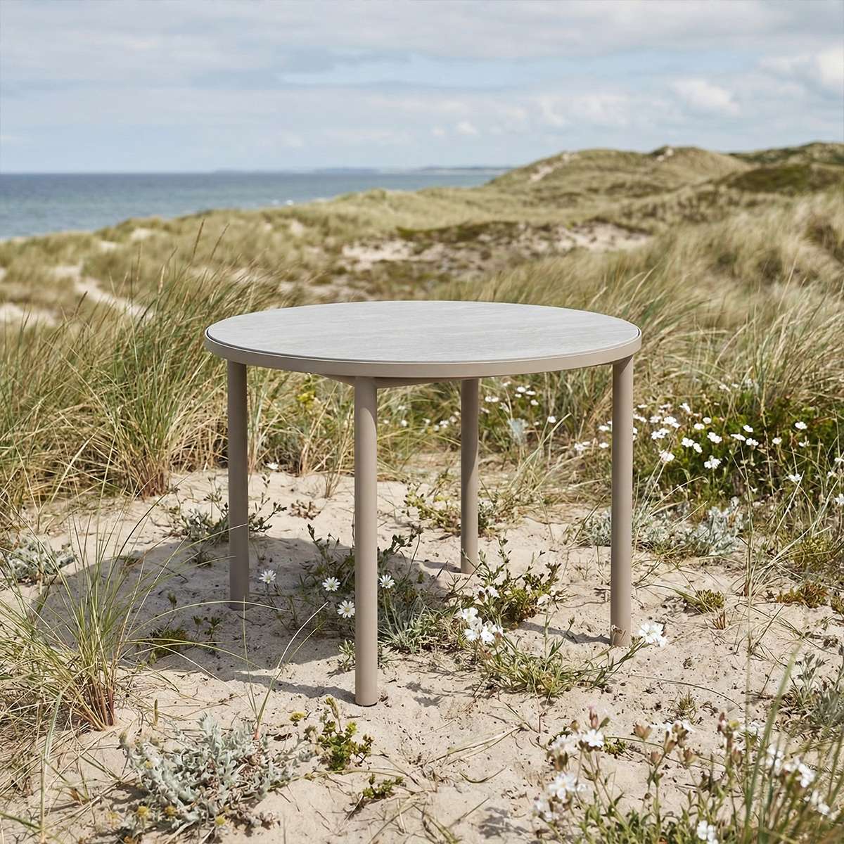 Round taupe Kirra Dining Table with teak wood top and powder-coated aluminum frame outdoors.