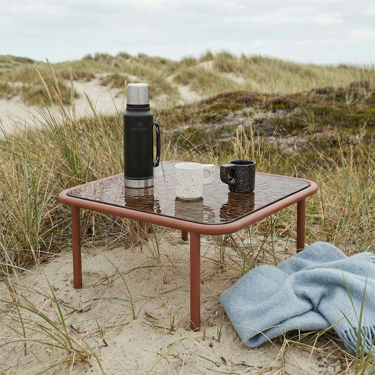 Square Mollis Coffee Table in chestnut with powder-coated aluminum frame and smoked tempered glass top outdoors.