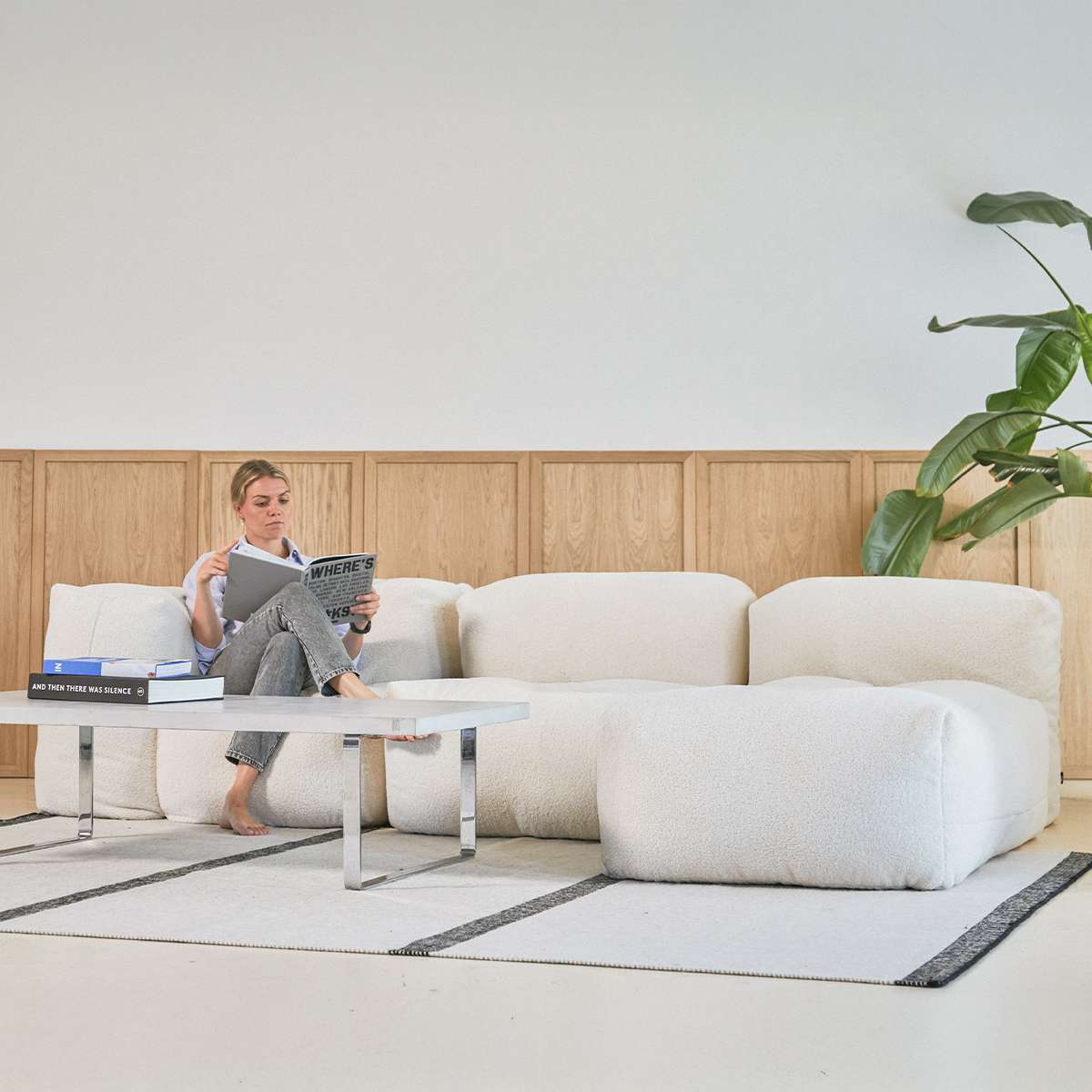 Cream indoor sofa with rounded cushions beside a coffee table and plant in a bright Scandinavian living room from sackit