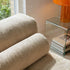 Close view of a beige corduroy Soft Sofa Indoor lounger with rounded cushions beside a glass side table and orange lamp in a bright home interior by sackit